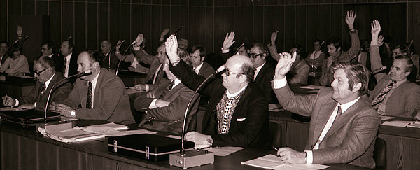 Personen in einem Sitzungsraum bei einer Abstimmung